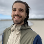Andrew is standing on a beach smiling at the camera.